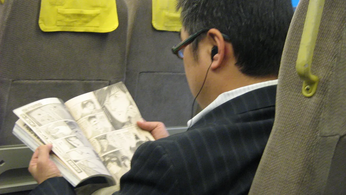 A commuter reading a printed manga magazine on a Japanese train