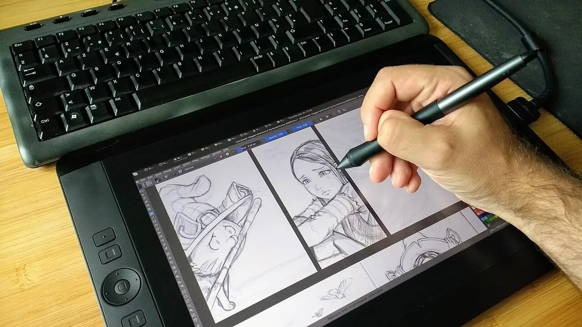 An artists hand penciling anime-style sketches on a Wacom Cintiq pen display next to a keyboard